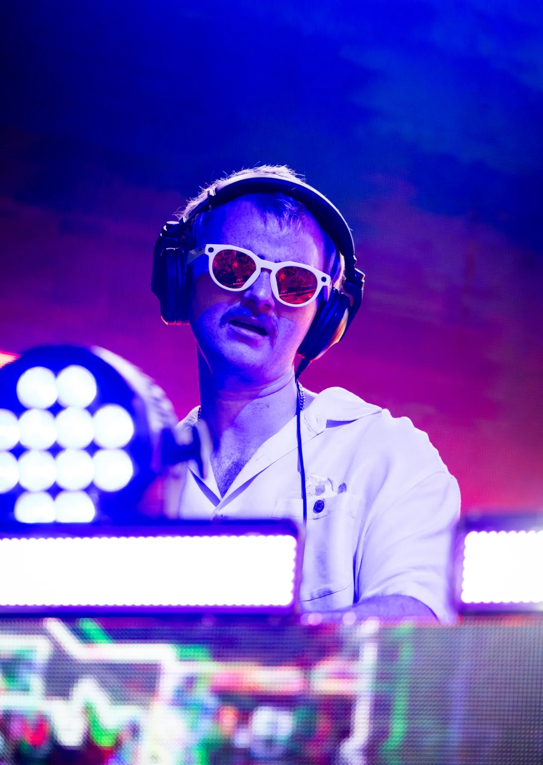 Close-up portrait of TITAN in white sunglasses and headphones under purple and blue stage lights