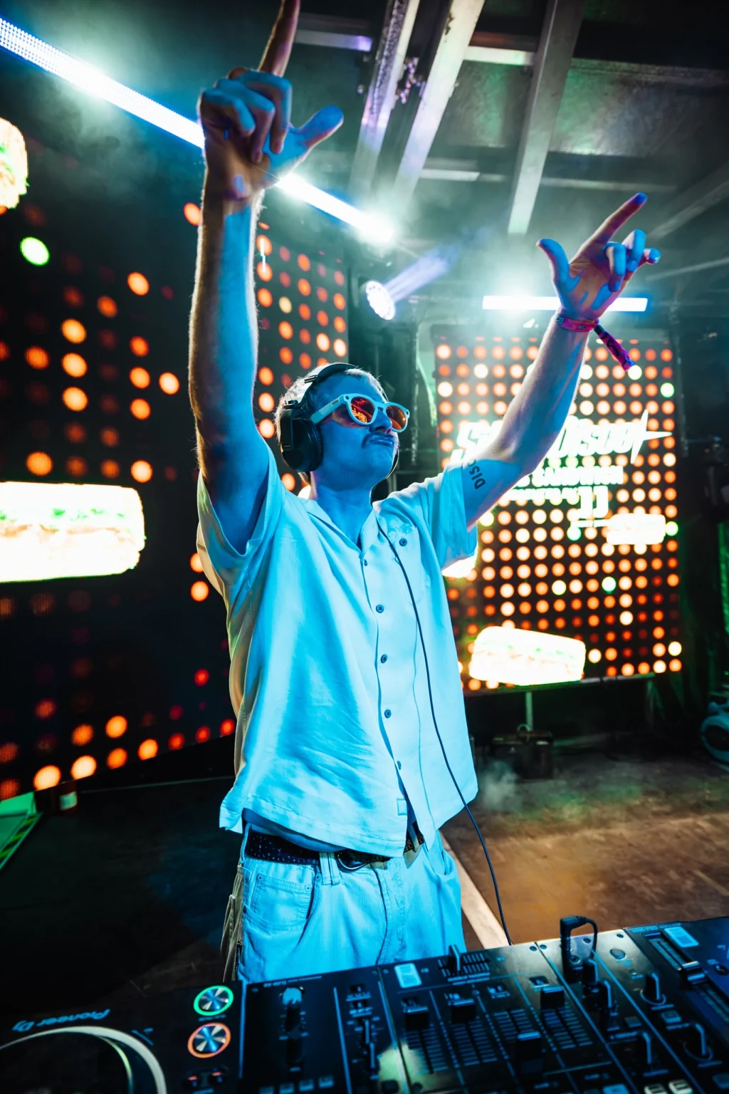 TITAN with both arms raised behind the decks under blue stage lights